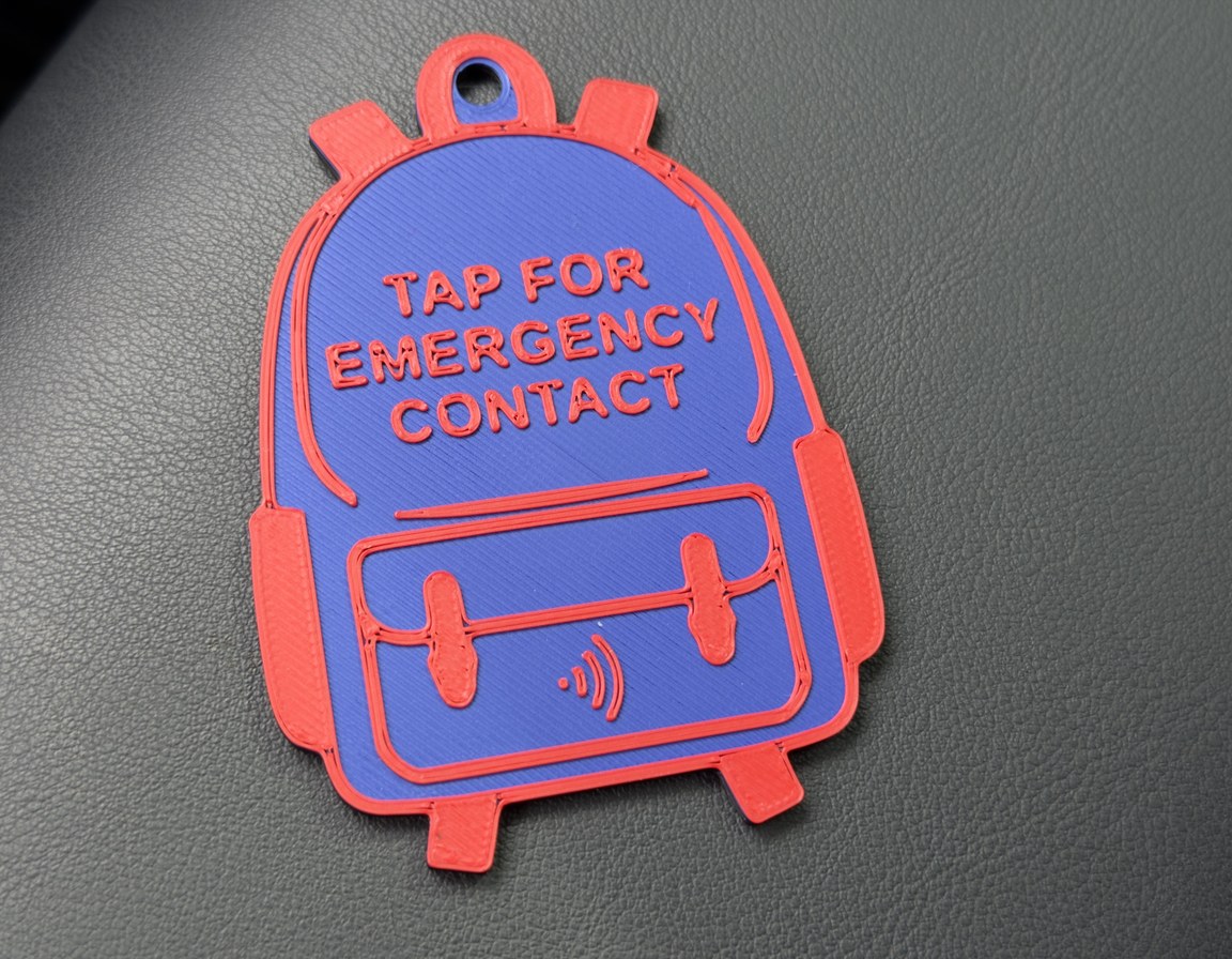 Blue backpack-shaped tag with TAP FOR EMERGENCY CONTACT and the tap mark raised in red