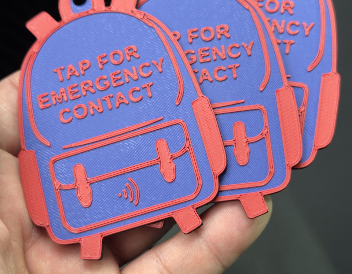 Three backpack tags fanned out in a hand, showing the tag is about as wide as four fingers