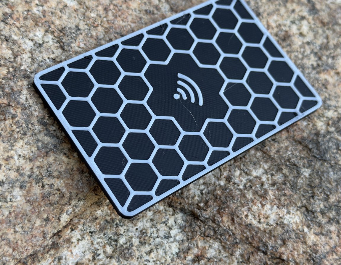 Black Replegend card with a raised white honeycomb face and the tap mark in the centre, on granite