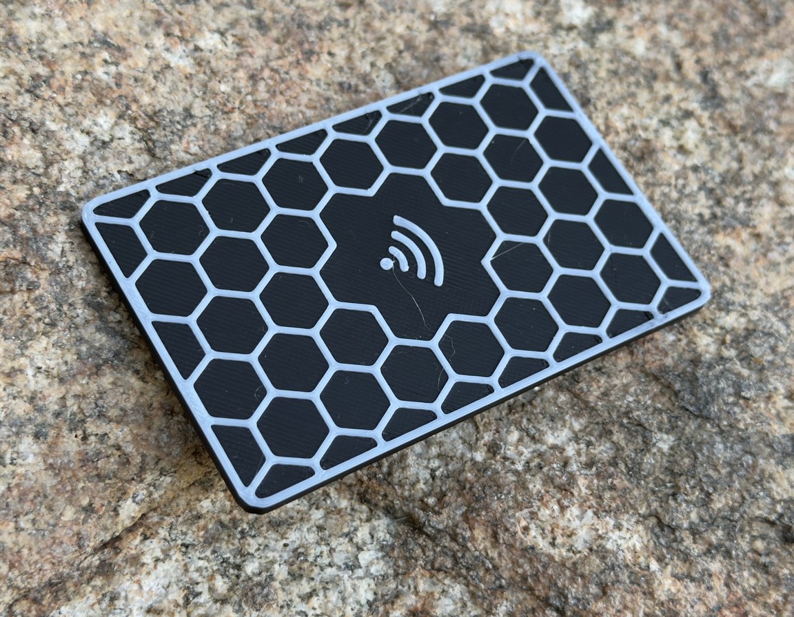 Black Replegend card on speckled granite at a three-quarter angle, the white comb walls standing proud of the recessed black cells, raised white tap mark near the centre