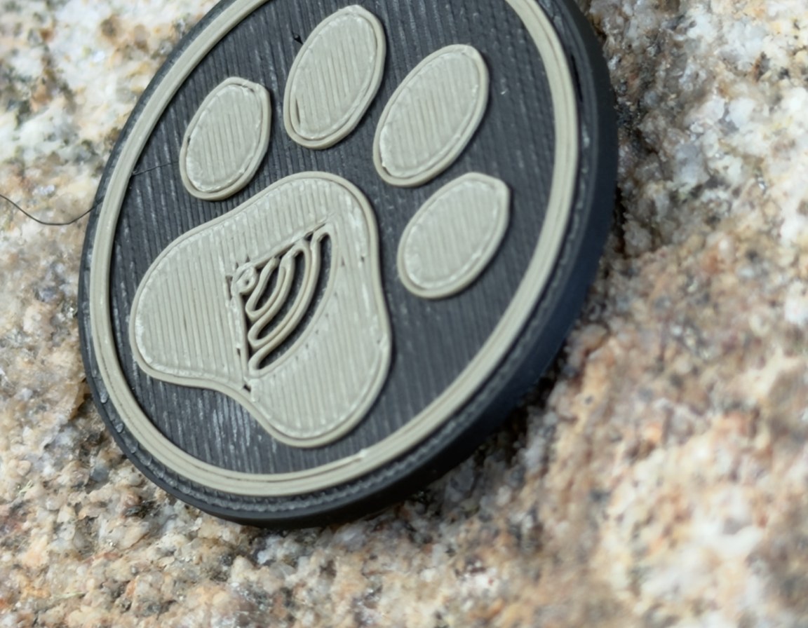 Black round paw tag with the paw, edge ring and tap mark raised in tan, close on granite