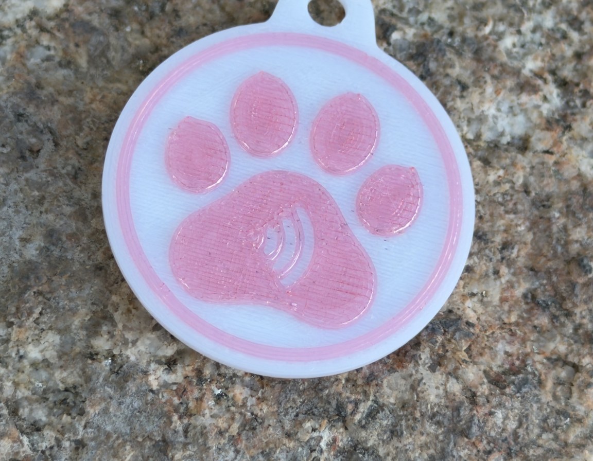 White round paw tag with the paw sunk into the face in pink, straight down on granite